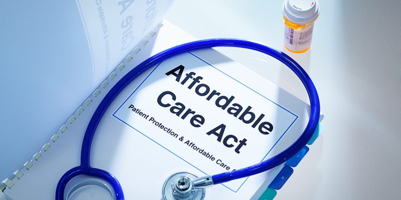 Still life of a manual handbook for the Patient Protection and Affordable Care Act with a stethoscope and prescription medication bottle. The manual is open to the title page, The open enrollment of the Affordable Care Act of the United States offers a health insurance program for all the U.S. citizens across the country.